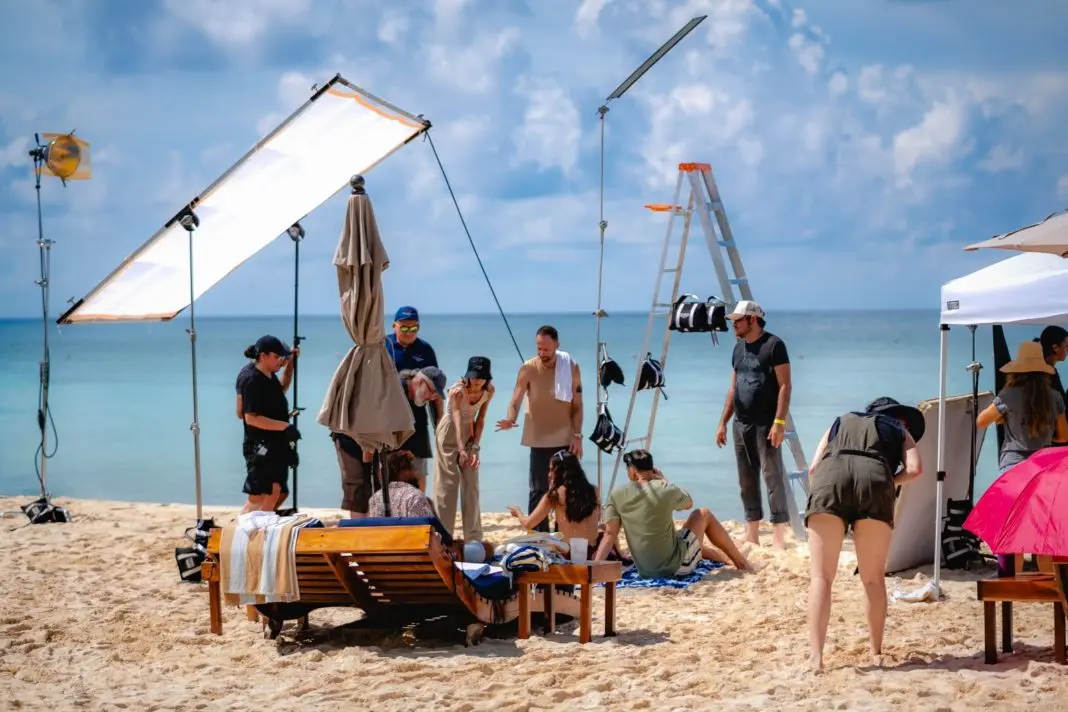 A group of people working on a beach photoshoot with lighting equipment and models-24102025