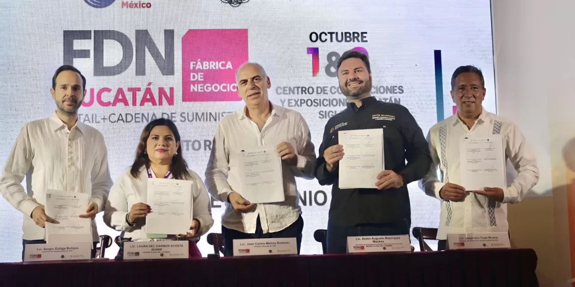 Five individuals holding signed documents during a business event in Yucatán, Mexico, with a banner in the background specifying details of the event.$# CAPTION