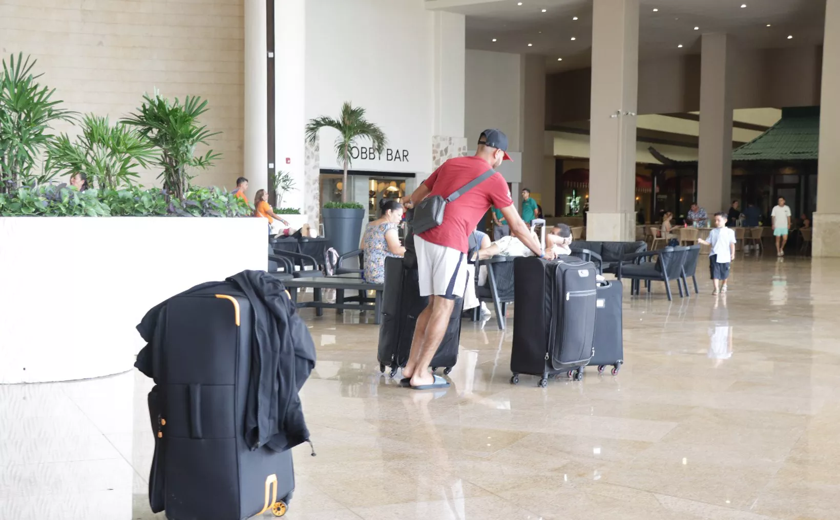 A man with luggage in a hotel lobby surrounded by other guests and plants