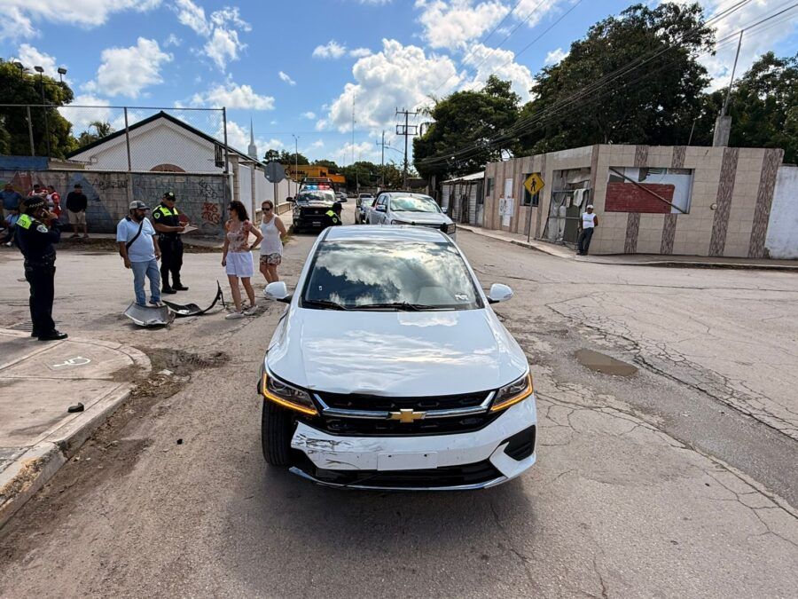 A white Chevrolet car with front-end damage at the scene of an accident, surrounded by people and police officers.$#$ CAPTION