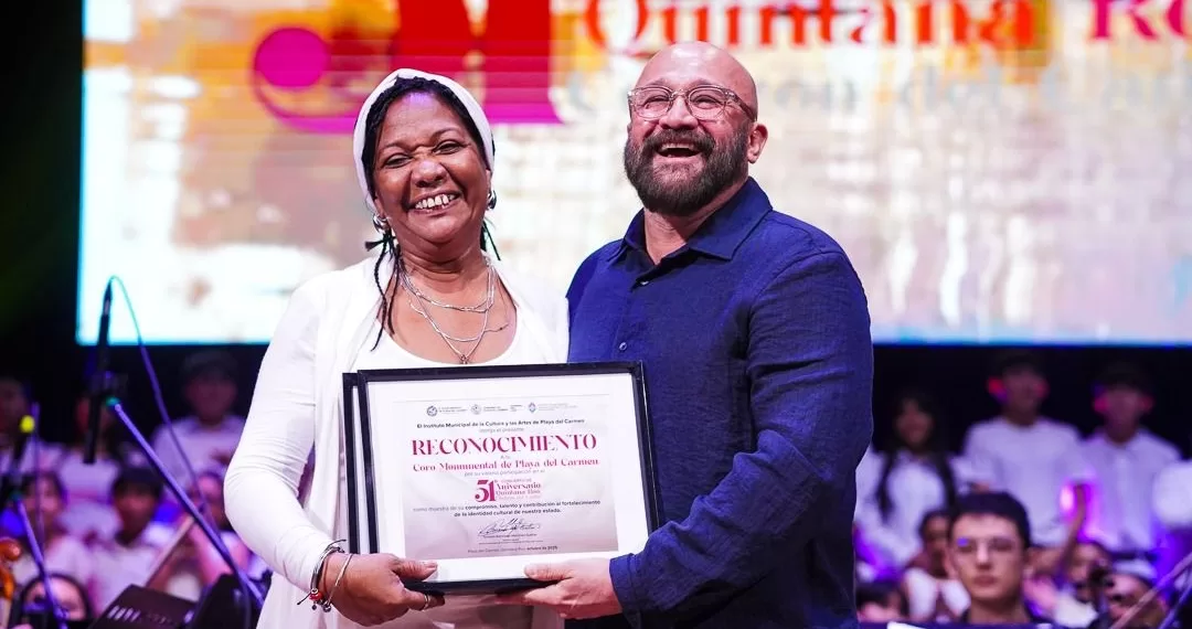 Two individuals smiling while holding a recognition certificate on stage during an event.$# CAPTION