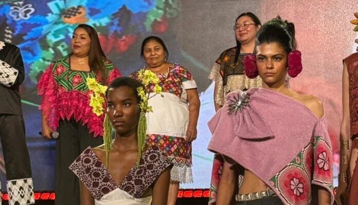 A fashion show featuring models in vibrant traditional clothing, with several women standing in the background, showcasing cultural attire and intricate designs.$# CAPTION
