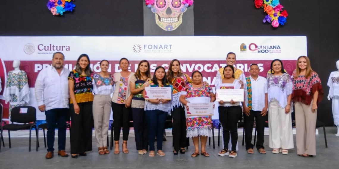 A group of individuals holding awards and certificates at a cultural event in Quintana Roo, with colorful traditional clothing and decorations in the background.$# CAPTION