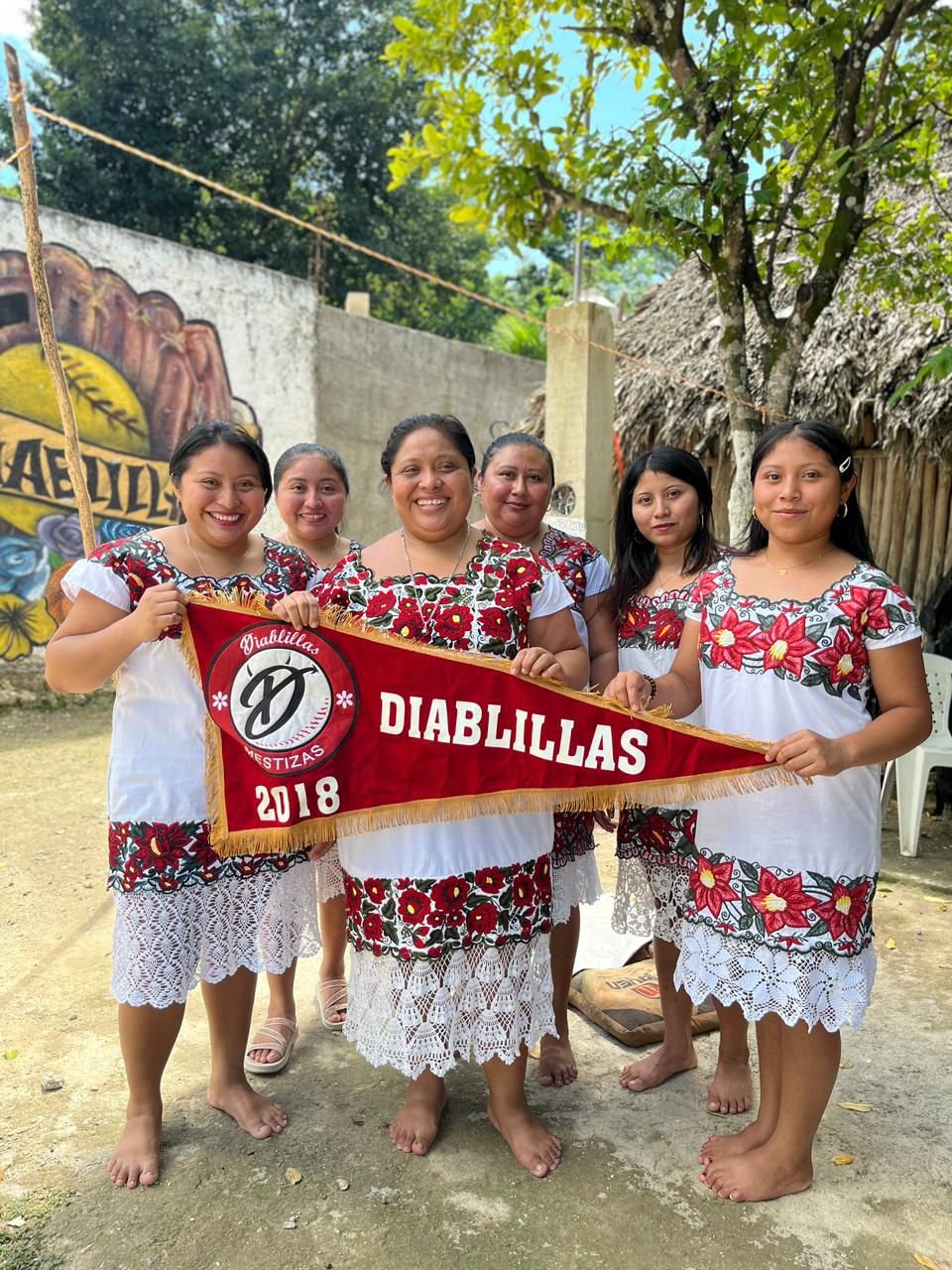 group of six women in traditional dresses holding a red banner in a vibrant outdoor setting