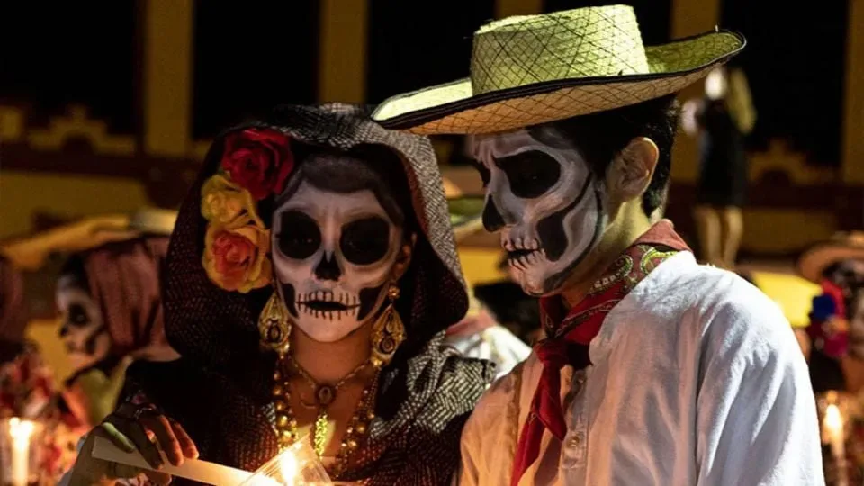 two people with skull face paint dressed in traditional attire during a festival at night