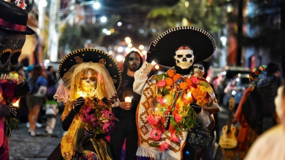 people dressed as skeletal figures celebrating in a vibrant nighttime parade with candles and flowers