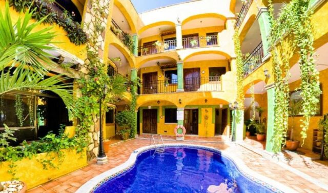 A vibrant courtyard with a swimming pool surrounded by yellow walls and lush greenery.$# CAPTION