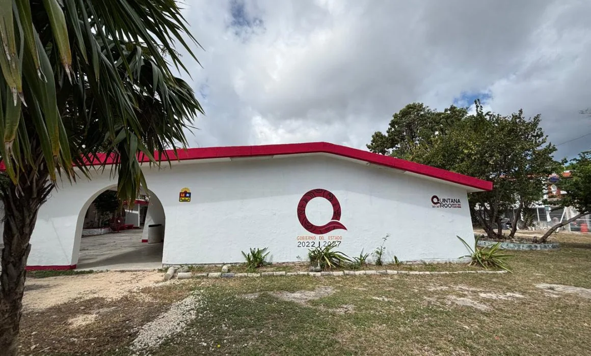 Exterior view of a white building with a red roof, featuring a circular logo and landscaping around it.$#$ CAPTION