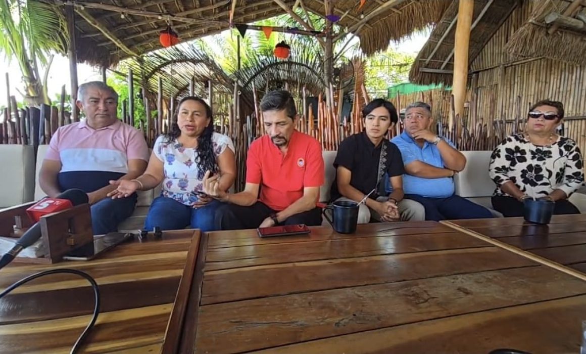 A group of community leaders sitting together in a casual setting, engaged in a discussion, surrounded by tropical decor.