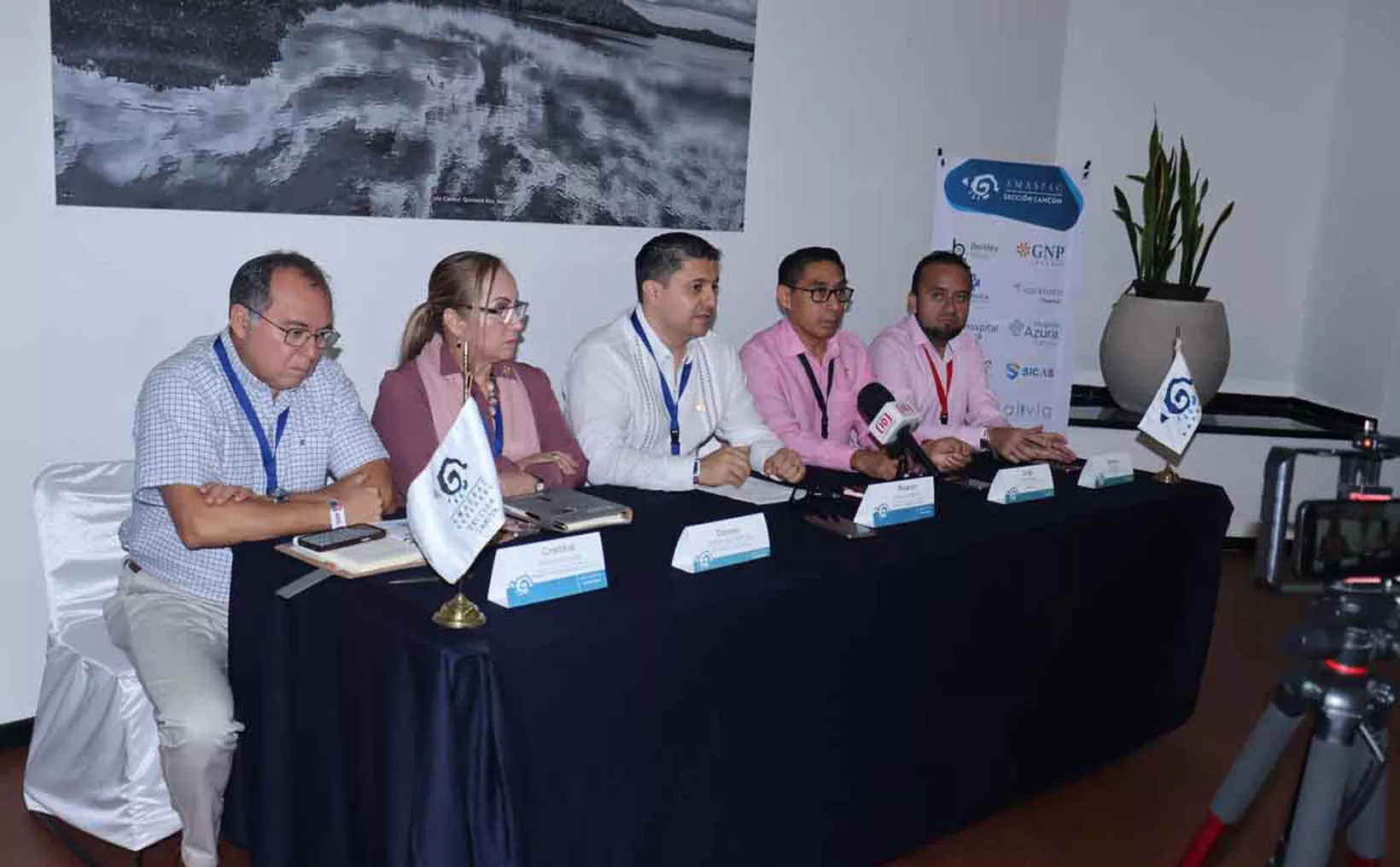 A panel of five individuals seated at a table during a conference discussion, with flags and nameplates displayed.$# CAPTION