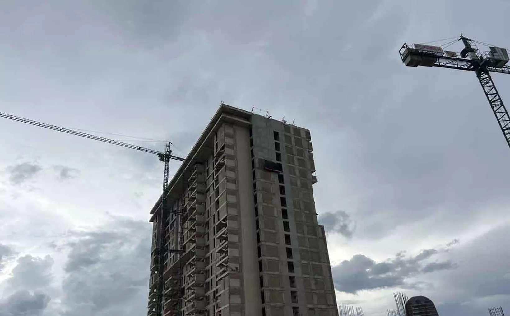 A towering unfinished high-rise building with a construction crane against a cloudy sky