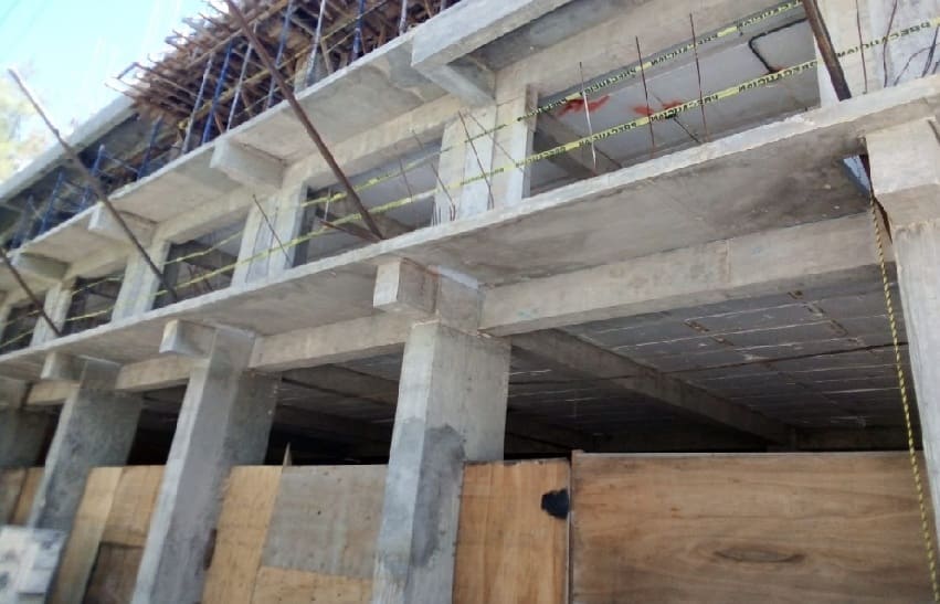 Exterior view of a concrete structure under construction with scaffolding and wooden barriers.