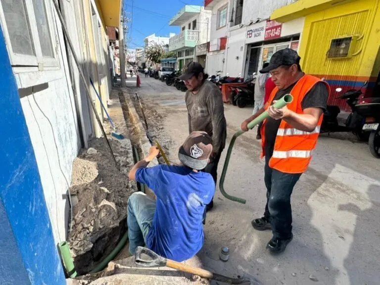 Three workers engaged in plumbing tasks alongside a street with parked scooters visible in the background