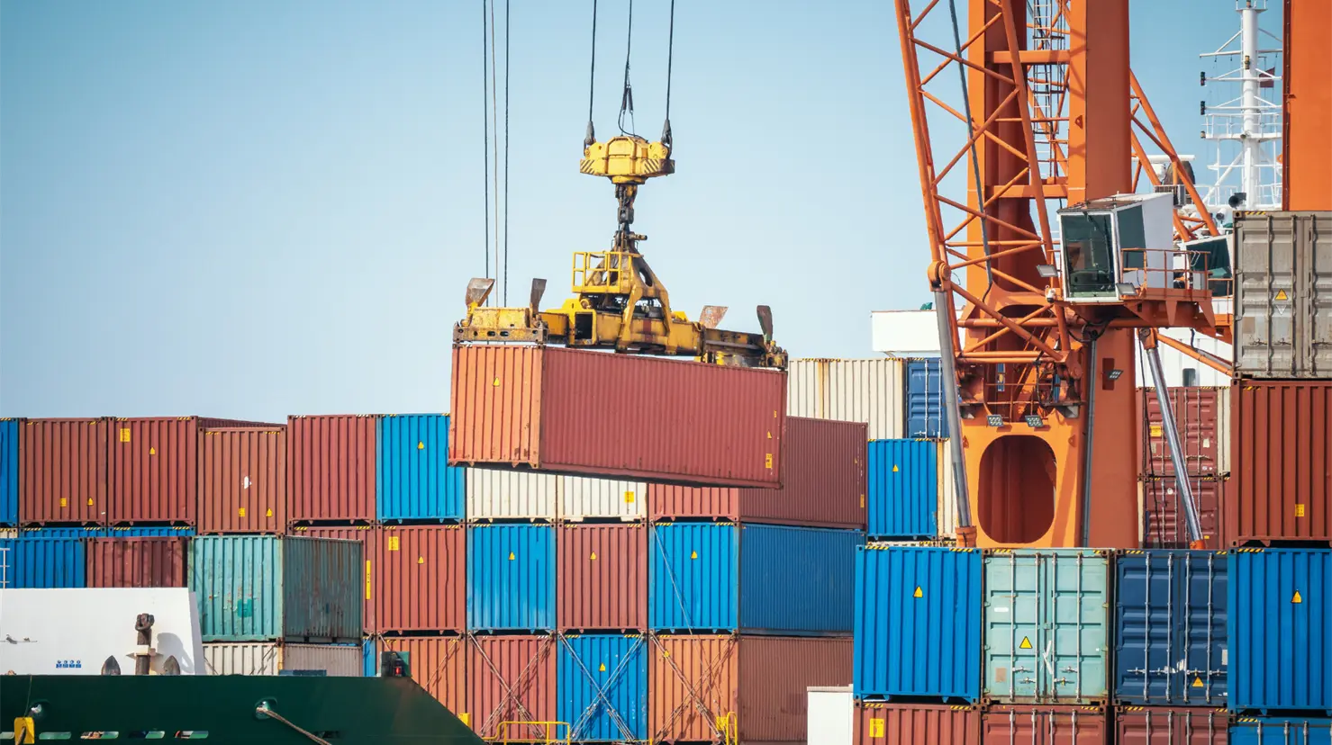 A crane lifting a shipping container at a port, surrounded by stacked colorful containers in the background.$# CAPTION