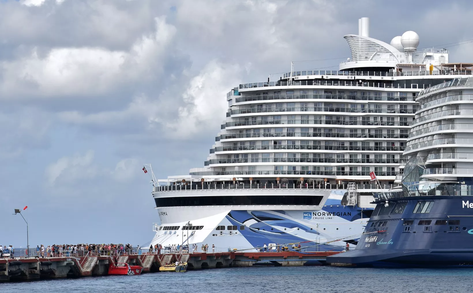Two large cruise ships docked at a bustling port with people waiting on the pier.$# CAPTION