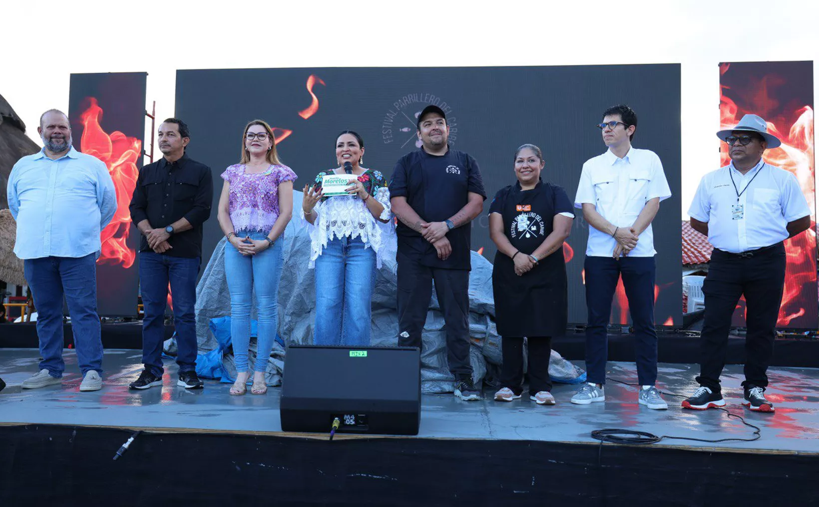 A group of people standing on stage at a culinary festival, with flames displayed on screens behind them. One person is holding an award.