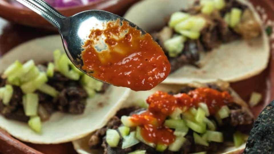 a spoonful of red salsa above tacos filled with meat and chopped vegetables