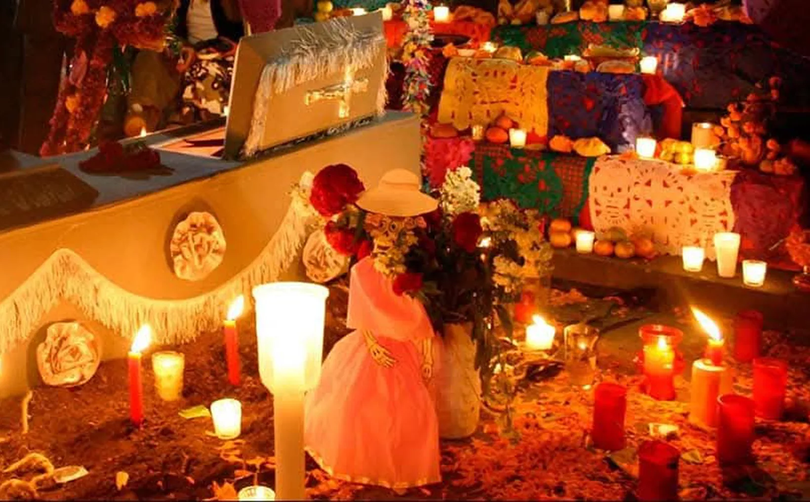 An altar adorned with candles, flowers, and a decorative skeleton doll, representing the Day of the Dead celebration, with vibrant decorations in the background.$# CAPTION