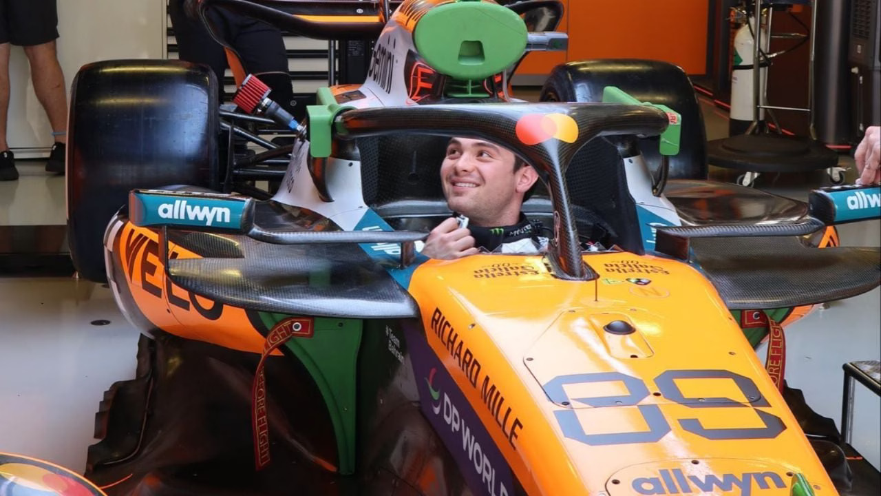 a smiling driver sitting in a Formula One car in a garage setting$# CAPTION