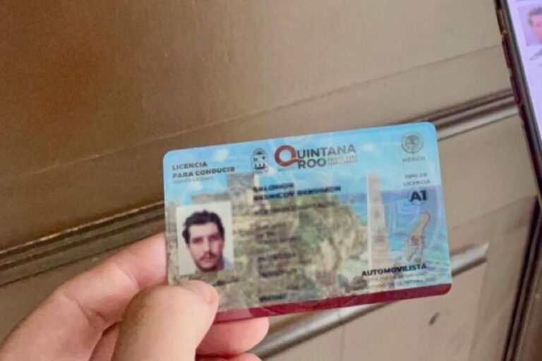 A hand holding a driving license from Quintana Roo, Mexico, showing a photo and personal details on a blue background.$# CAPTION