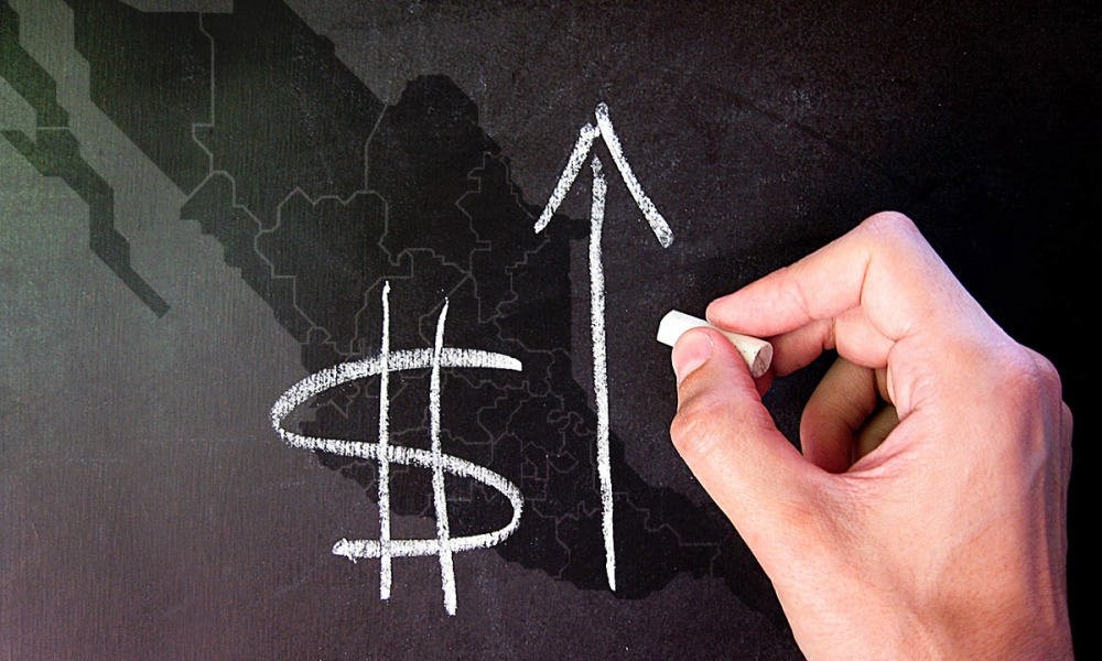 A hand drawing a dollar sign and an upward arrow on a chalkboard.