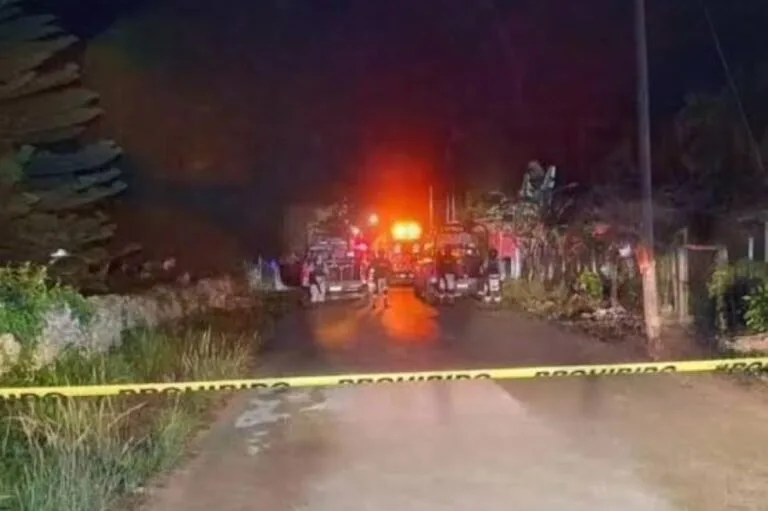 A night scene showing emergency vehicles and personnel behind police tape on a dimly lit street with greenery along the side.$# CAPTION