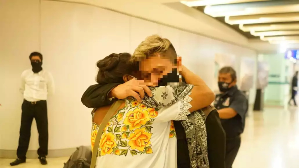 Two individuals embrace in an emotional reunion at an airport, wearing face masks.$# CAPTION