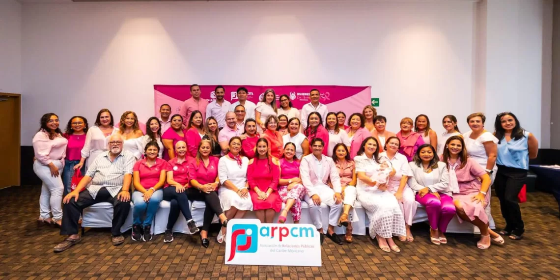 A large group of individuals in pink attire posing for a photo at an event, with a banner in the background representing ARPCM.$# CAPTION
