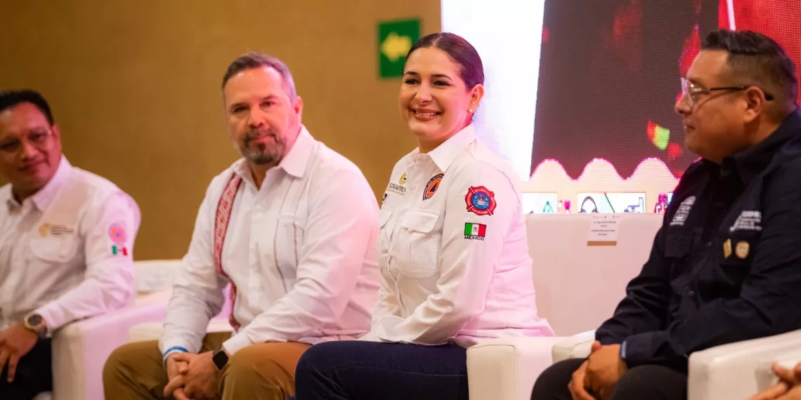 Four officials participating in a panel discussion, seated on stage with a large screen behind them.$# CAPTION