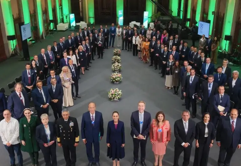 a large group of people dressed in formal attire gathered around floral arrangements in a well-lit indoor venue