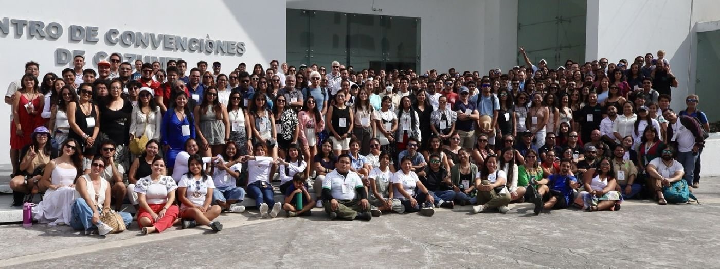 A large group of people standing together in front of a convention center, smiling and posing for a photo.$# CAPTION