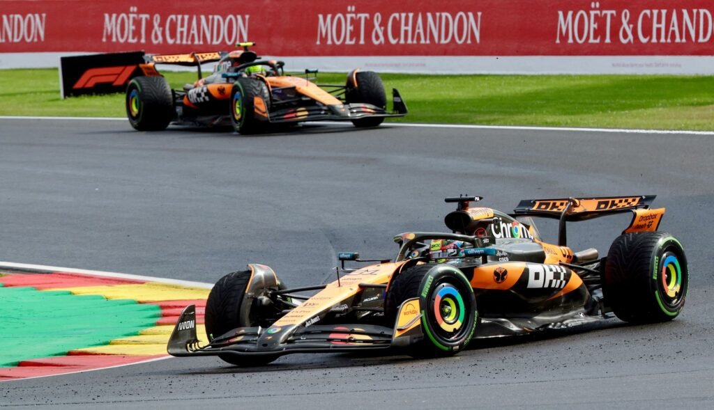 Two Formula 1 cars racing on a track with colorful pit lane signage in the background