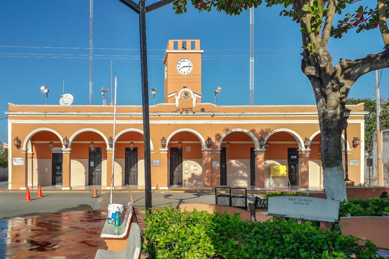 A historic building featuring a clock tower, arched entrances, and surrounded by greenery under a clear blue sky.$#$ CAPTION