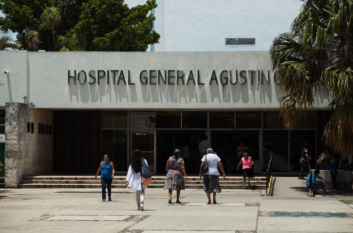 A group of people walking towards the entrance of Hospital General Agustin on a sunny day with greenery around