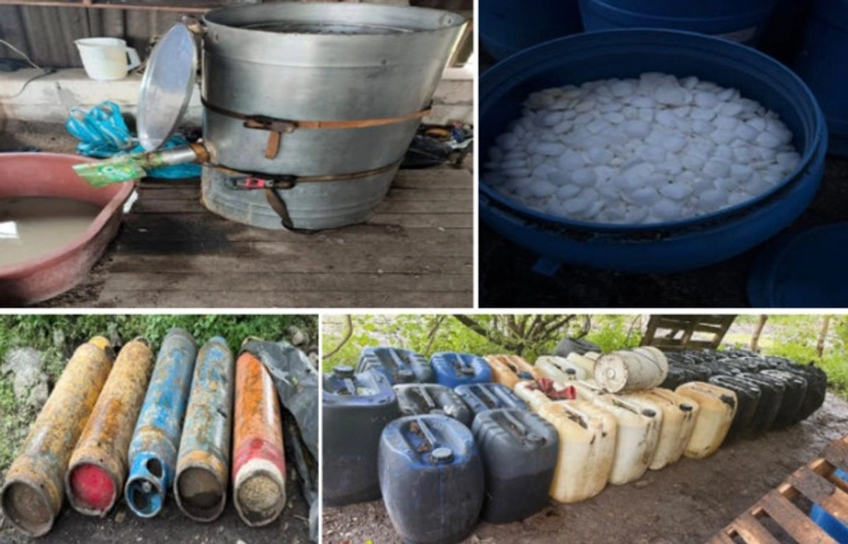 Various containers and equipment associated with illegal distillation, including a large metal barrel and several plastic drums and canisters, situated in a rustic environment.