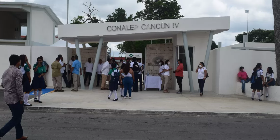 A group of students and attendees at the entrance of CONALEP Cancun IV, a technical education institution, with people mingling and a banner overhead.$# CAPTION
