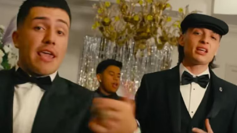 two men in tuxedos performing during a festive event with a third person in the background
