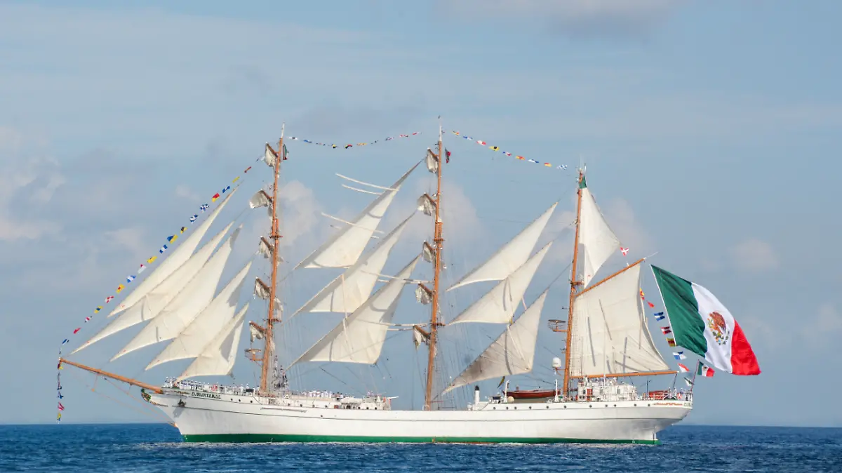 A tall ship with multiple sails and a Mexican flag flying, sailing on the open sea under a blue sky.$# CAPTION