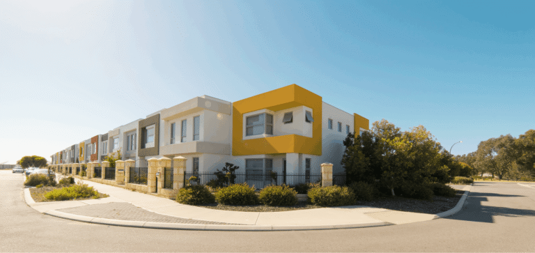 A row of modern houses featuring colorful design elements, surrounded by greenery and a clear blue sky