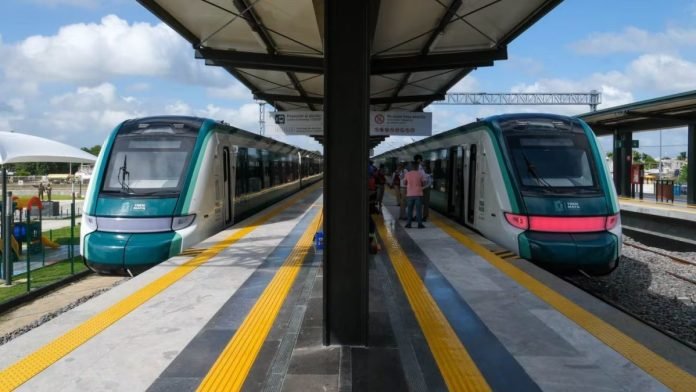 Two trains at a modern station with yellow safety lines and passengers on platforms under a clear blue sky