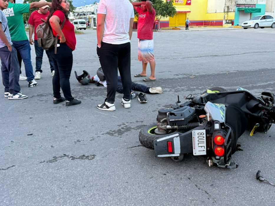 A group of people gathered around a motorcycle accident on the street, with one person lying on the ground and the motorcycle overturned nearby.$#$ CAPTION