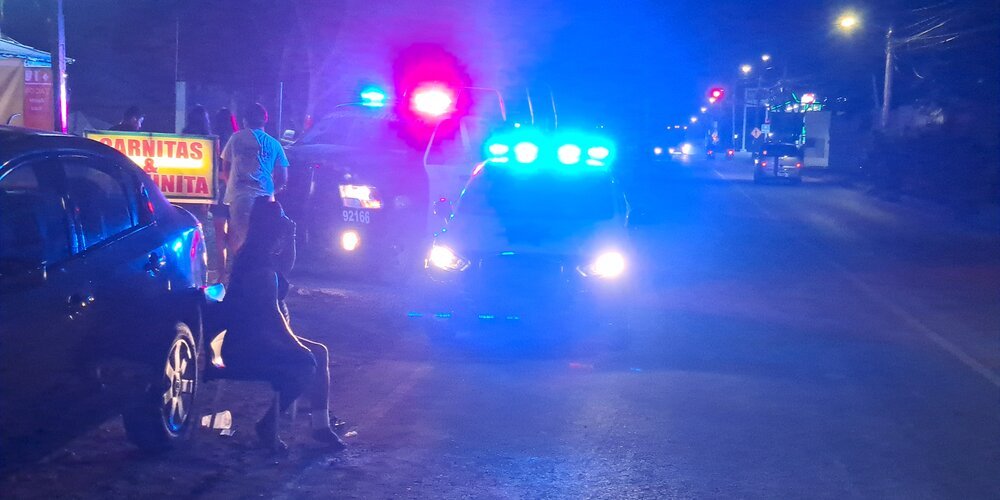 A scene at night showing police cars with flashing lights and people near a food stall on a street.$#$ CAPTION