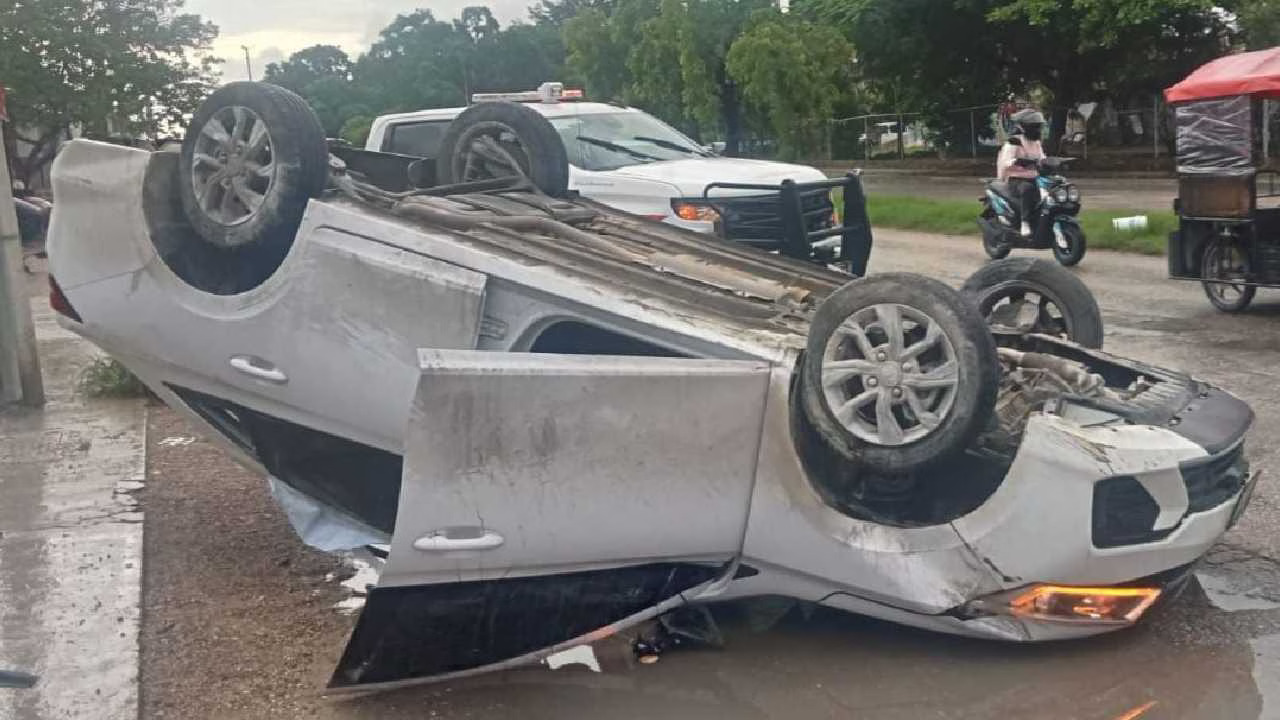 a white vehicle flipped upside down on a road surrounded by greenery and other vehicles
