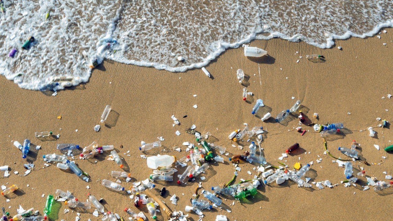 aerial view of plastic waste scattered on a sandy beach with waves approaching