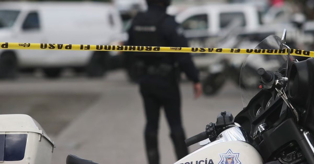 A police officer stands behind a yellow barricade tape at a crime scene, with a police motorcycle in the foreground