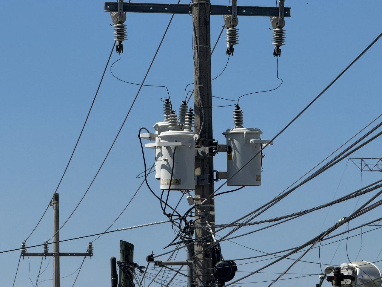 A utility pole features two transformers and several power lines under a blue sky