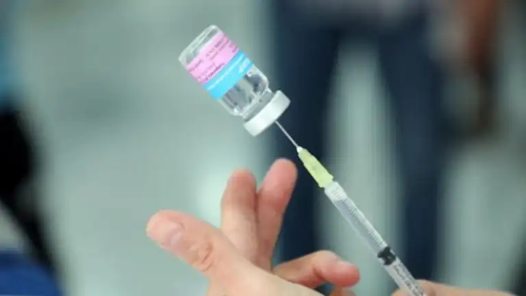 A hand holding a syringe poised to draw liquid from a vial of vaccine.$# CAPTION