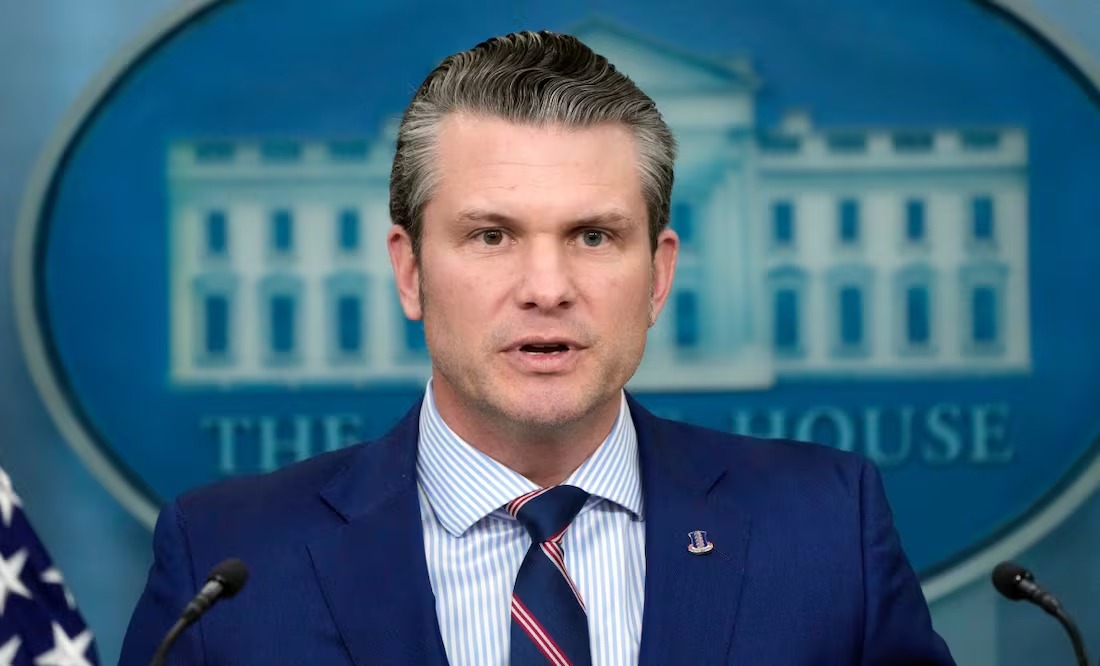 A man in formal attire speaking at a podium during a press briefing at the White House, with the presidential seal in the background.$# CAPTION
