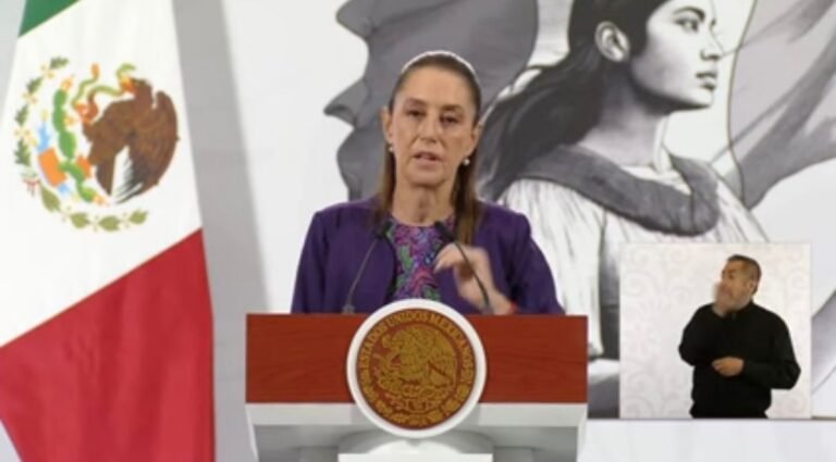 A woman speaking at a podium during a press conference, with the Mexican flag and a mural in the background. An interpreter is visible in the corner. $# CAPTION