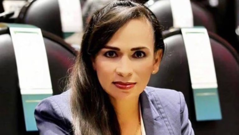 a woman with long hair wearing a suit sitting in a formal environment with chairs in the background